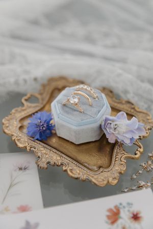 A delicate wedding ring box displayed on vintage paper frames with soft blue and floral decorative elements.