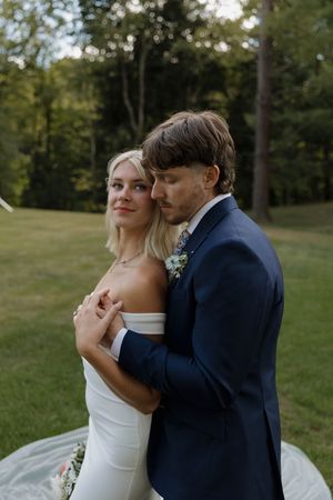 A couple in wedding attire share an intimate moment in a lush green outdoor setting at sunset.