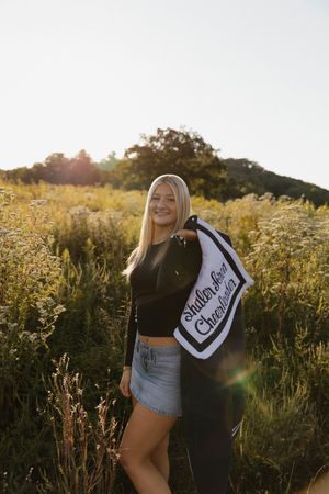 A person poses in golden late afternoon sunlight among tall grasses wearing denim shorts and a black top.