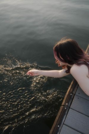 Someone reaches over the edge of a wooden boat to touch sparkling water on a moody overcast day at sea.