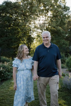 A couple holds hands and smiles while walking through a lush green garden at golden hour.