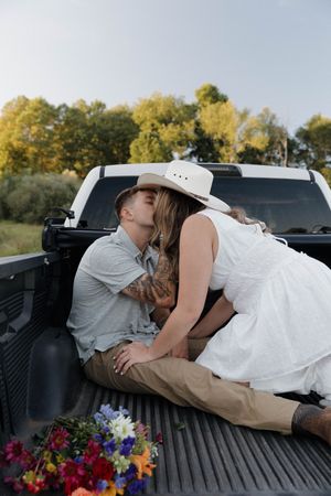 A romantic moment shared in the bed of a pickup truck with colorful flowers beside them on a sunny autumn day.
