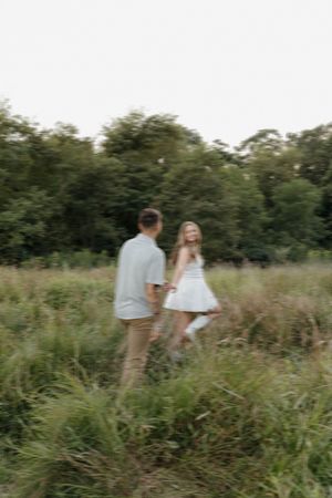 A couple shares a joyful moment together while walking through tall grass in a natural outdoor setting.