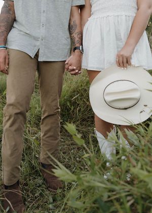 A close-up view of people's legs in khaki pants and light-colored dresses standing together in tall grass outdoors.