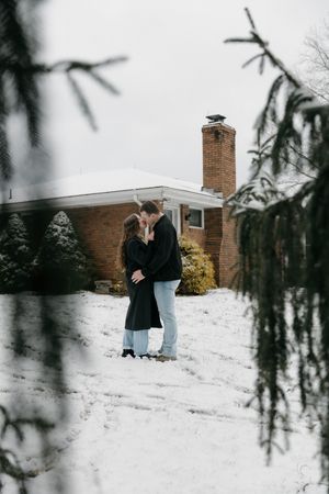 A winter engagement photoshoot in the snow with evergreen branches framing the romantic scene.
