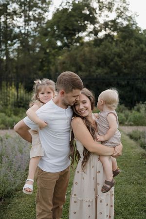 Happy young family with two toddlers embracing outdoors in a lush green garden setting.