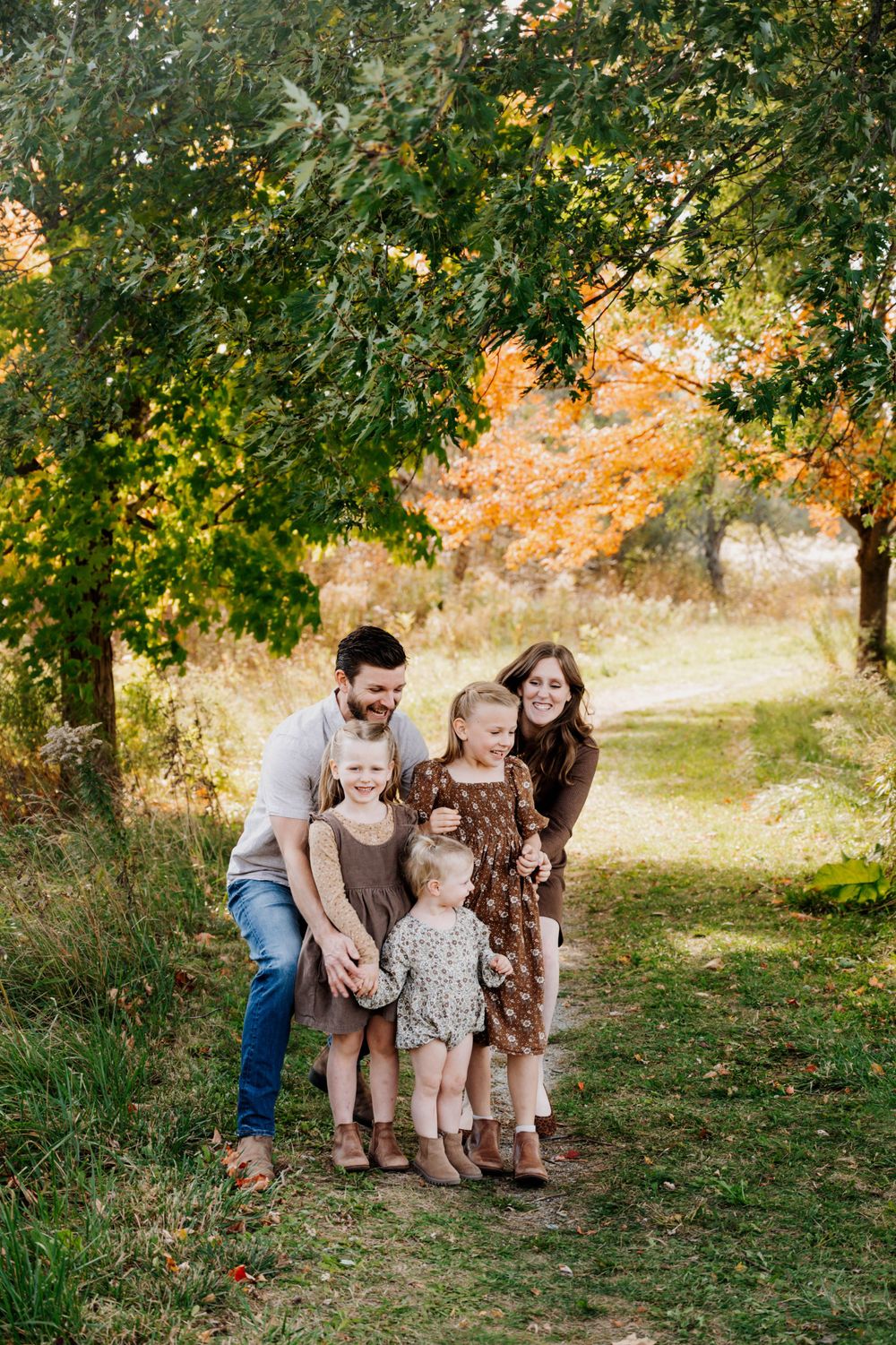 Family photo session on a tree-lined path during golden autumn weather.