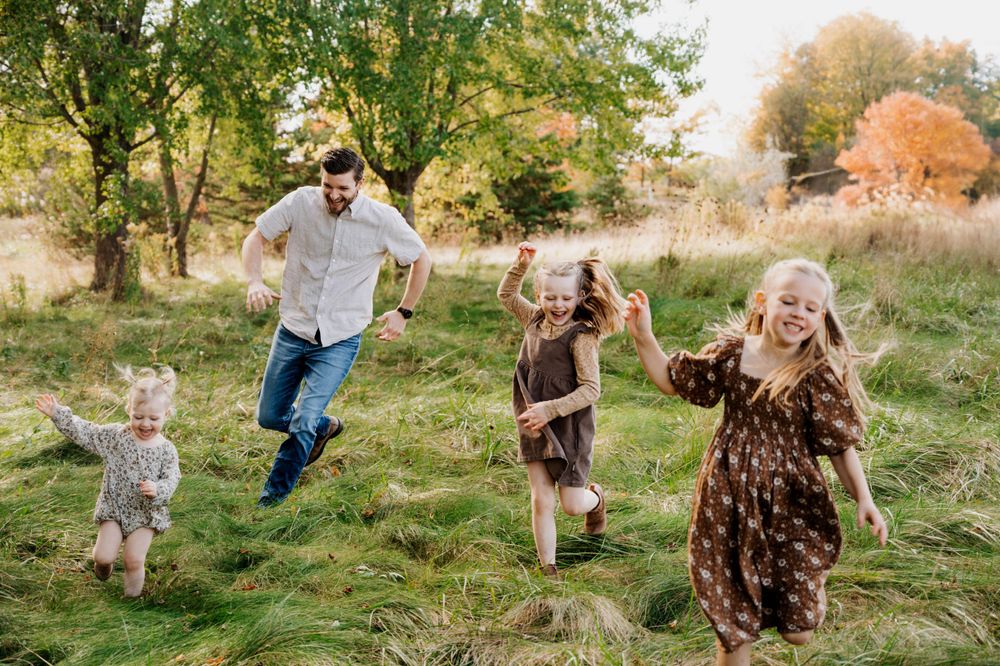 Family running and playing together in tall grass on sunny autumn day.