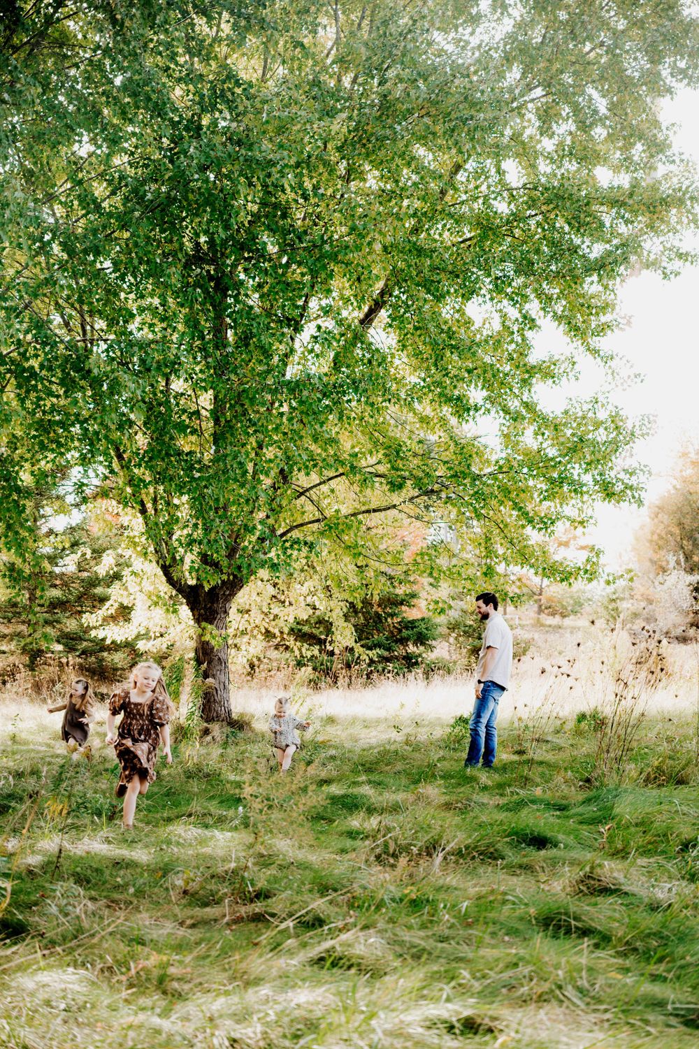 Family enjoying outdoor time under large tree in sunlit meadow.