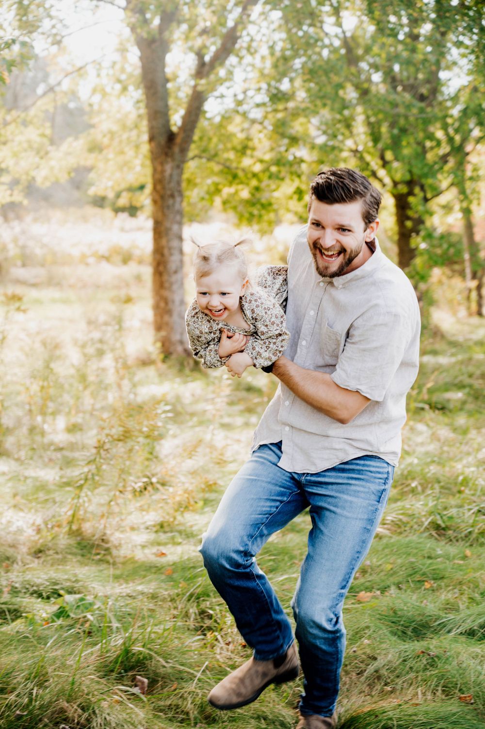 Playful moment in grassy field with parent swinging child during golden hour.