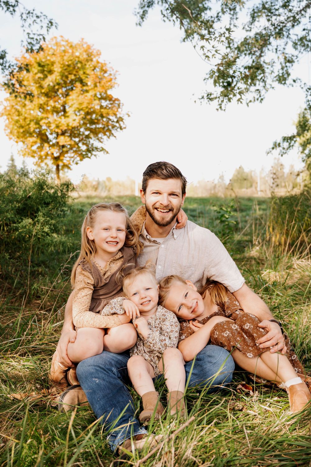 Casual outdoor family portrait in grassy field with autumn trees in background.