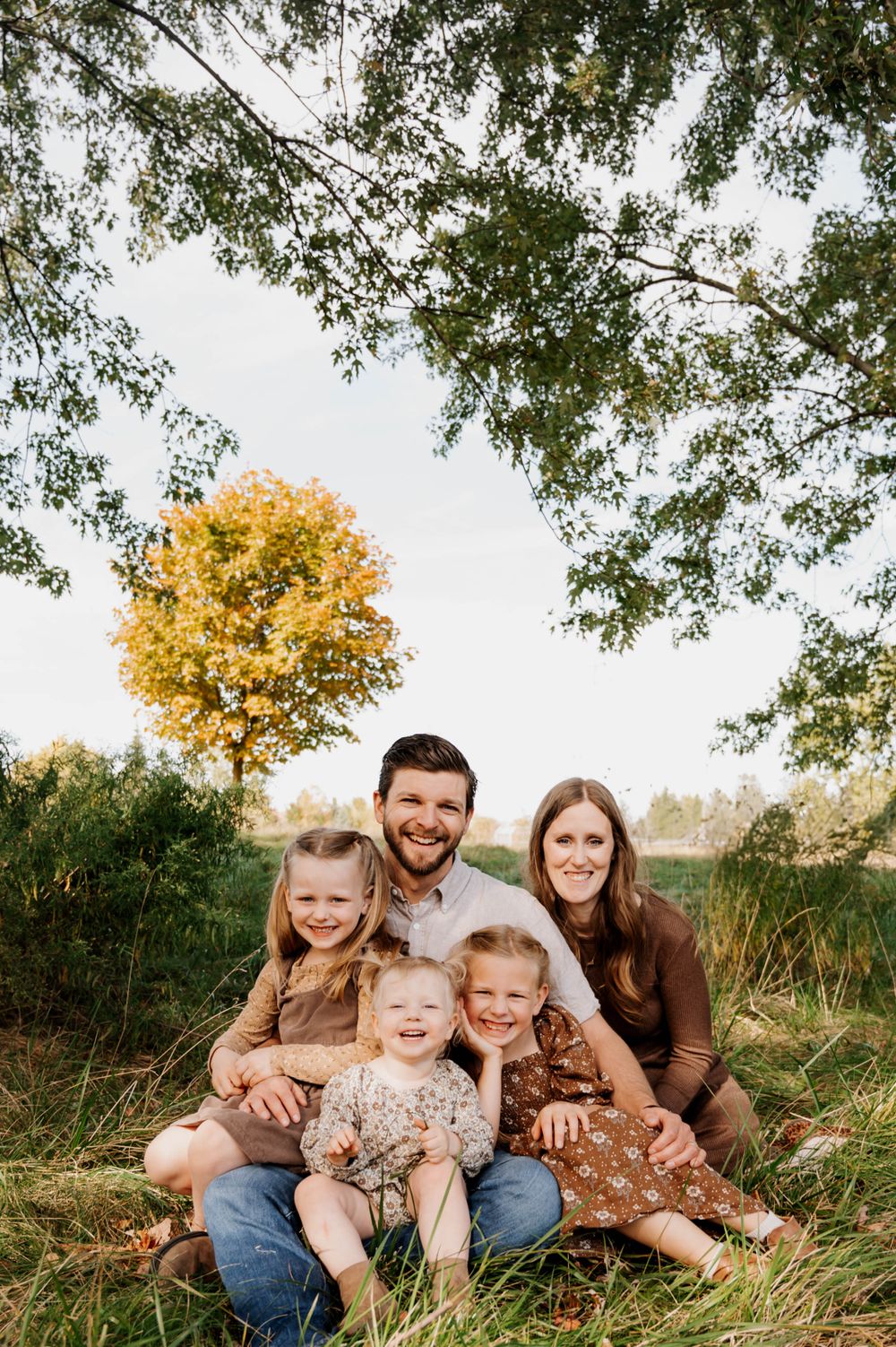 Family sitting together in tall grass with golden autumn tree in background.
