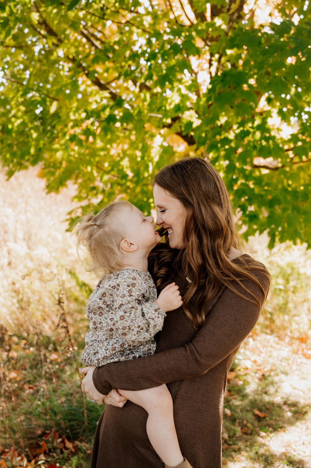 Tender moment between parent and child beneath autumn tree branches.