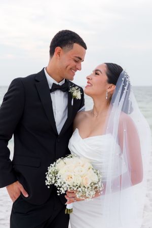 Wedding couple sharing intimate moment on beach with white bouquet.