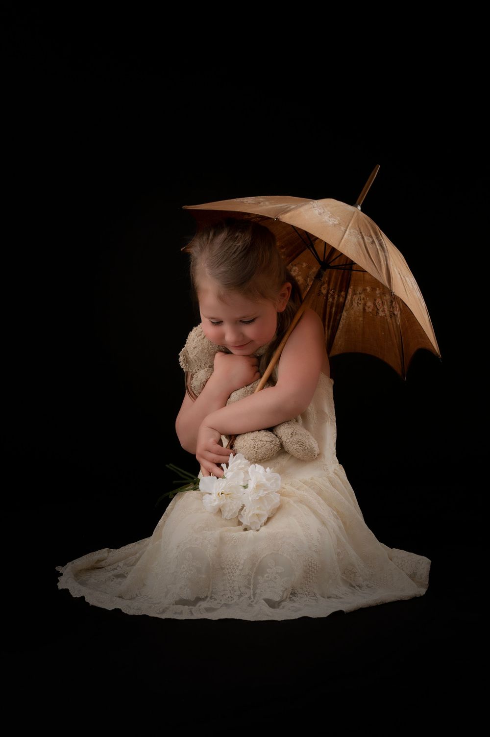 An artistic portrait with antique parasol and cream dress in dark setting.