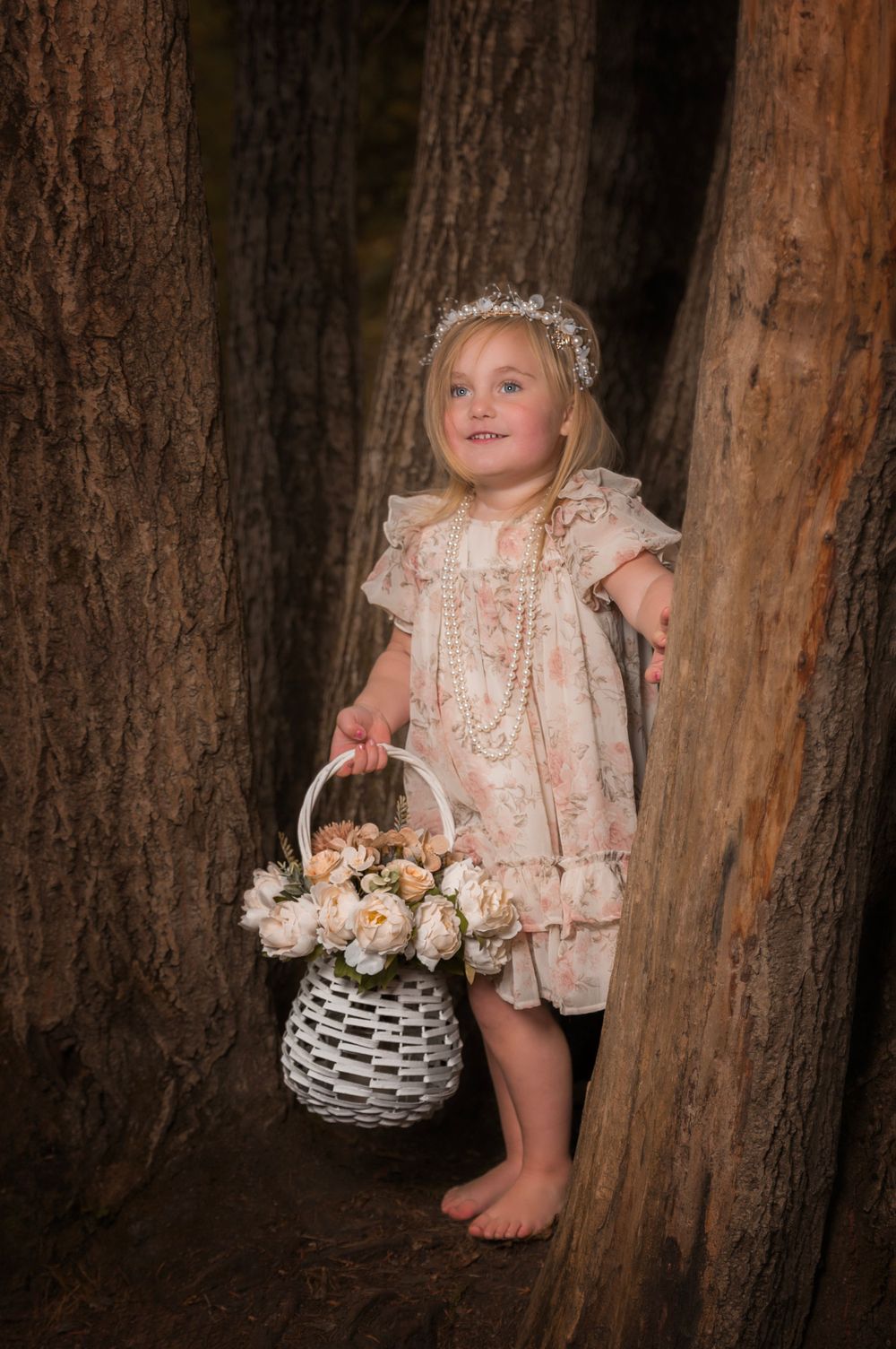 Whimsical portrait with white basket and lace dress against rustic tree backdrop.