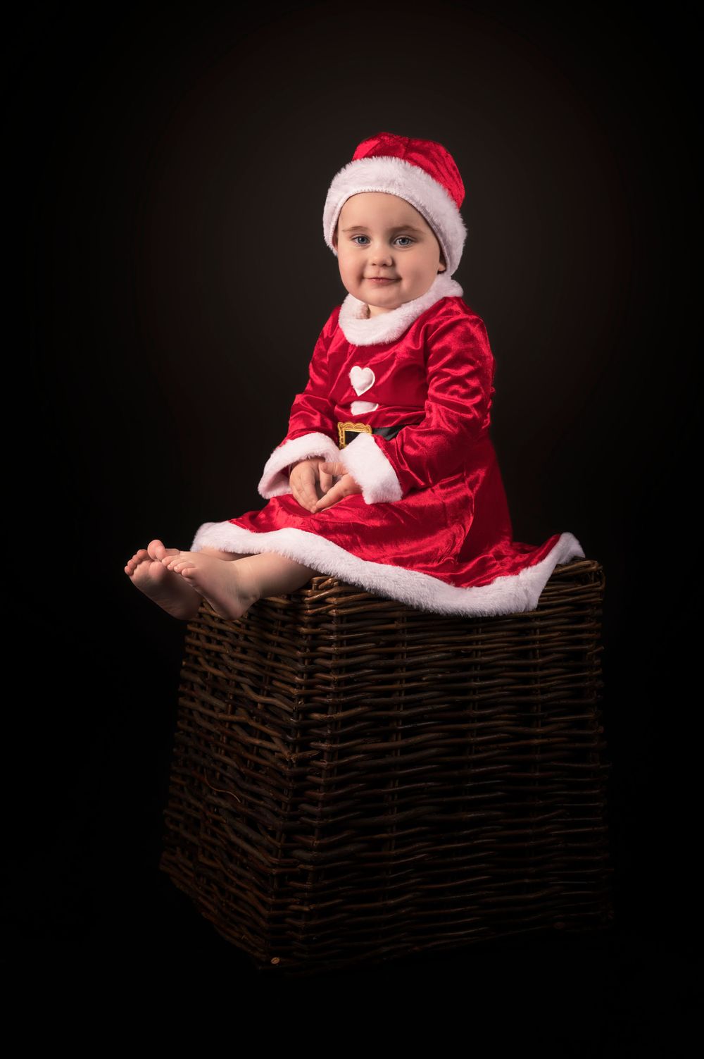 A holiday portrait featuring a Santa costume and wicker storage box.
