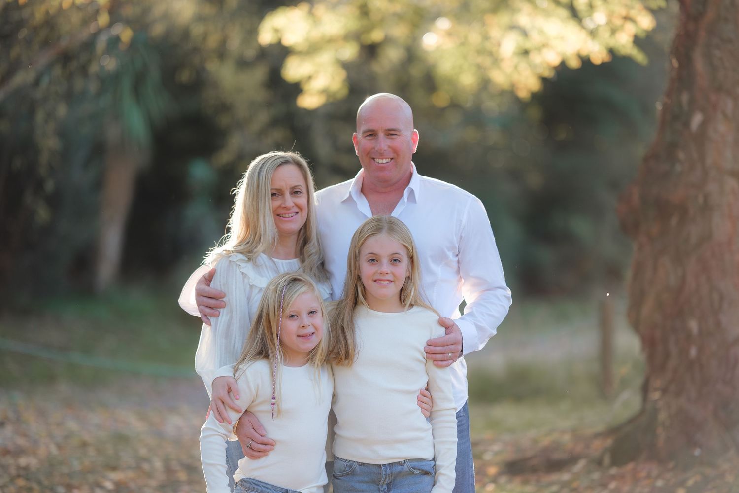 Family members gather for outdoor portraits among tall trees in natural lighting.