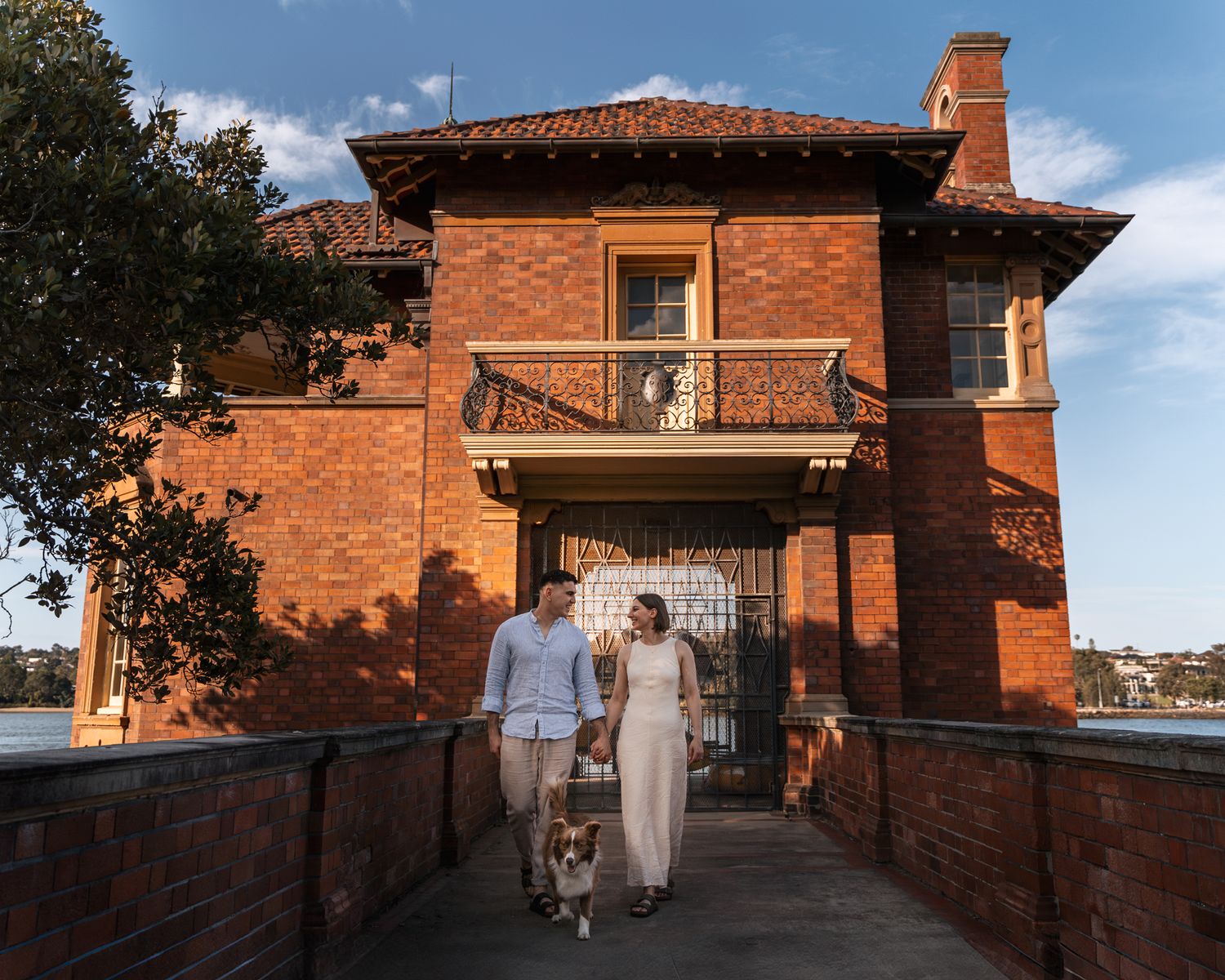 couple-walks-towards-camera-from-a-nice-building-together-with-their-puppy-during-engagement-photoshoot