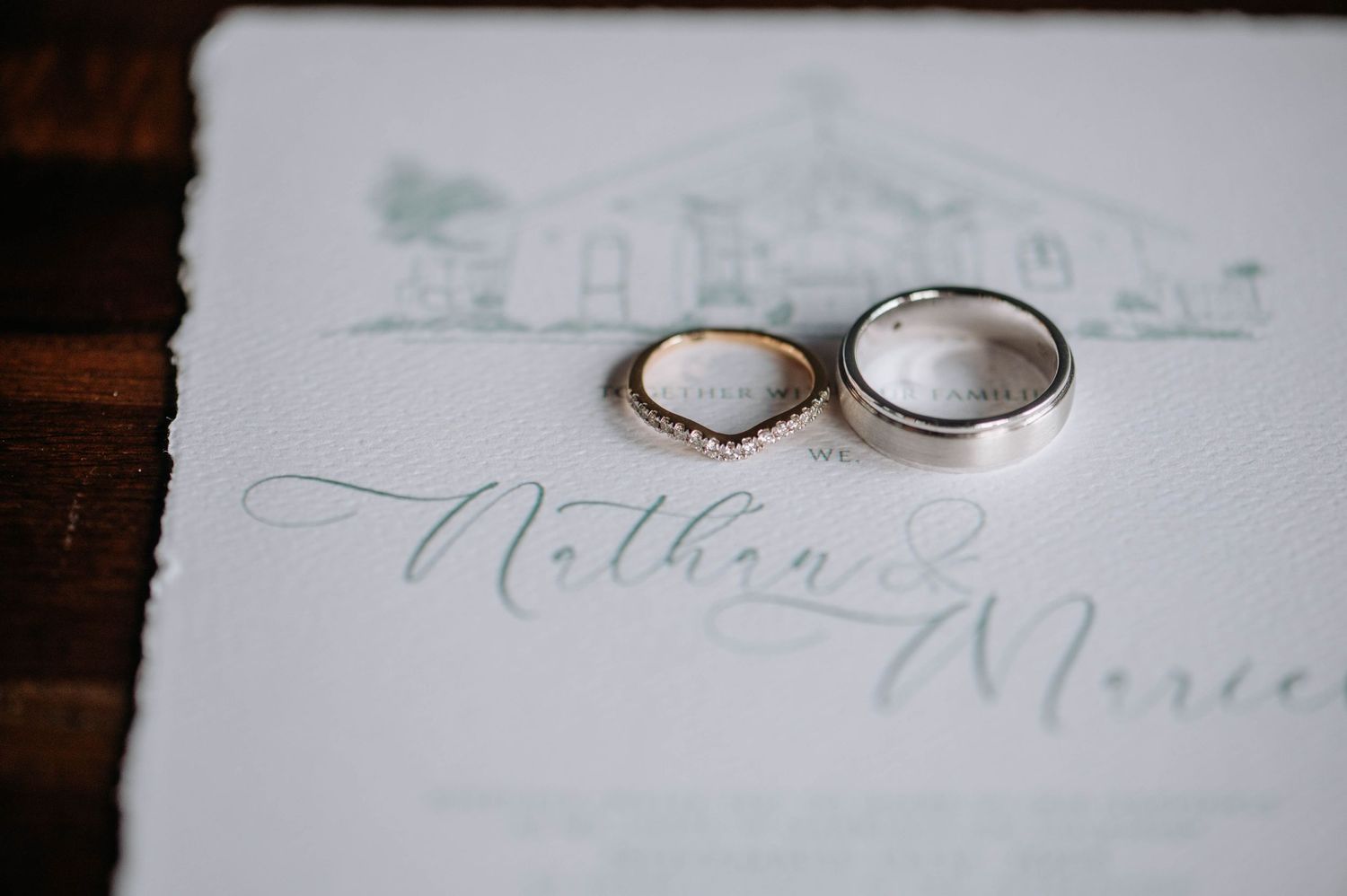 Wedding rings placed on a delicate invitation card with pale green architectural sketch details.
