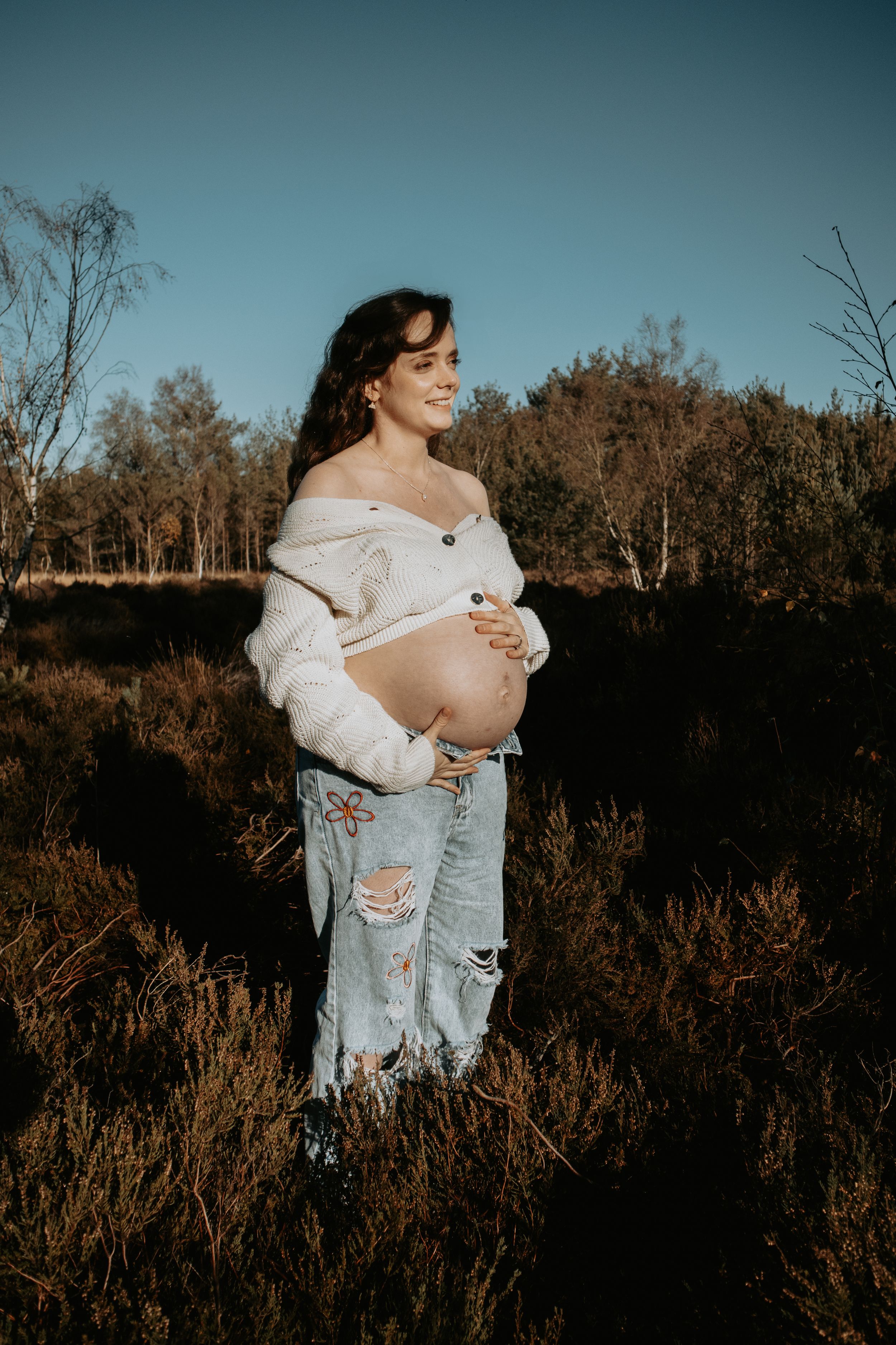 A maternity photoshoot in a natural outdoor setting during golden hour.