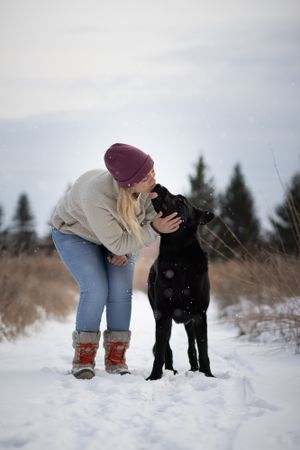 Person and black dog share a tender moment in snowy winter landscape.