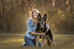 A German Shepherd dog and companion pose together in a warm golden outdoor setting at sunset.
