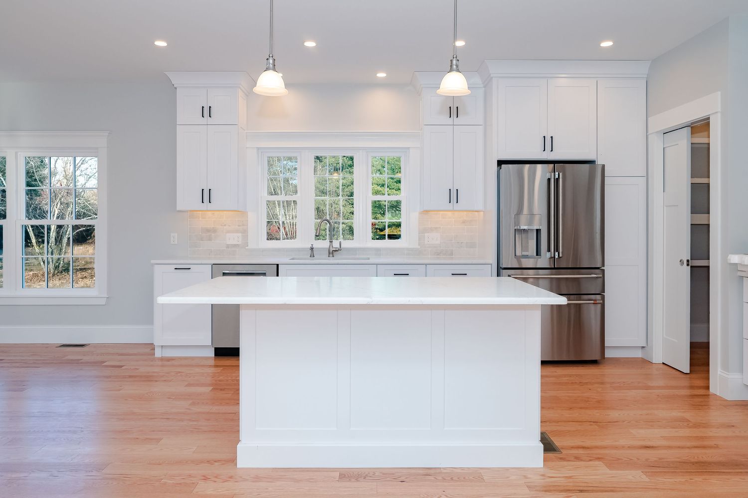Bright white modern kitchen with center island, hardwood floors and stainless steel appliances.