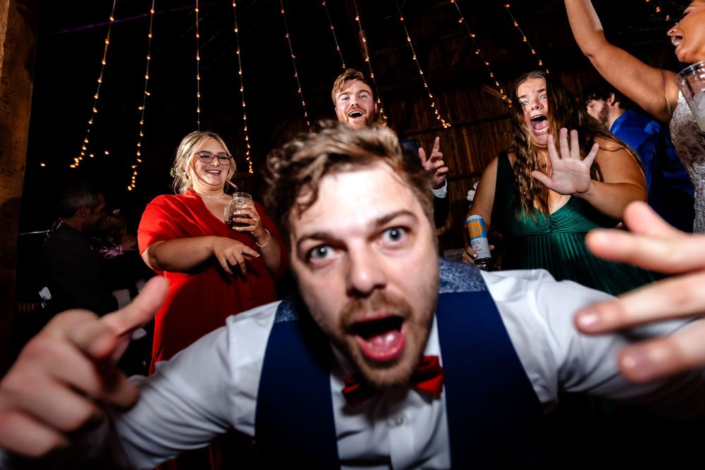 Energetic dancing and celebration captured in dimly lit barn reception.