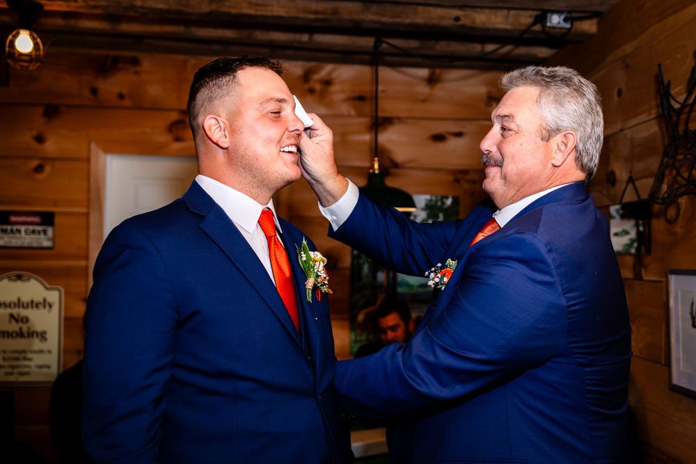 Candid moments between groomsmen in navy suits inside rustic wooden venue.