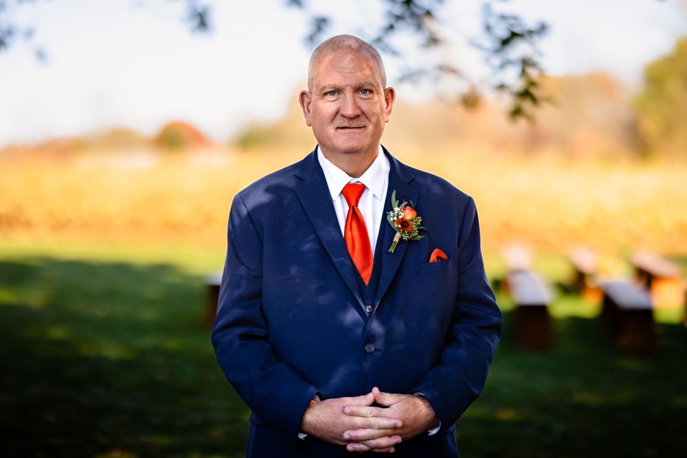 Wedding party in formal attire standing outdoors in autumn sunlight.