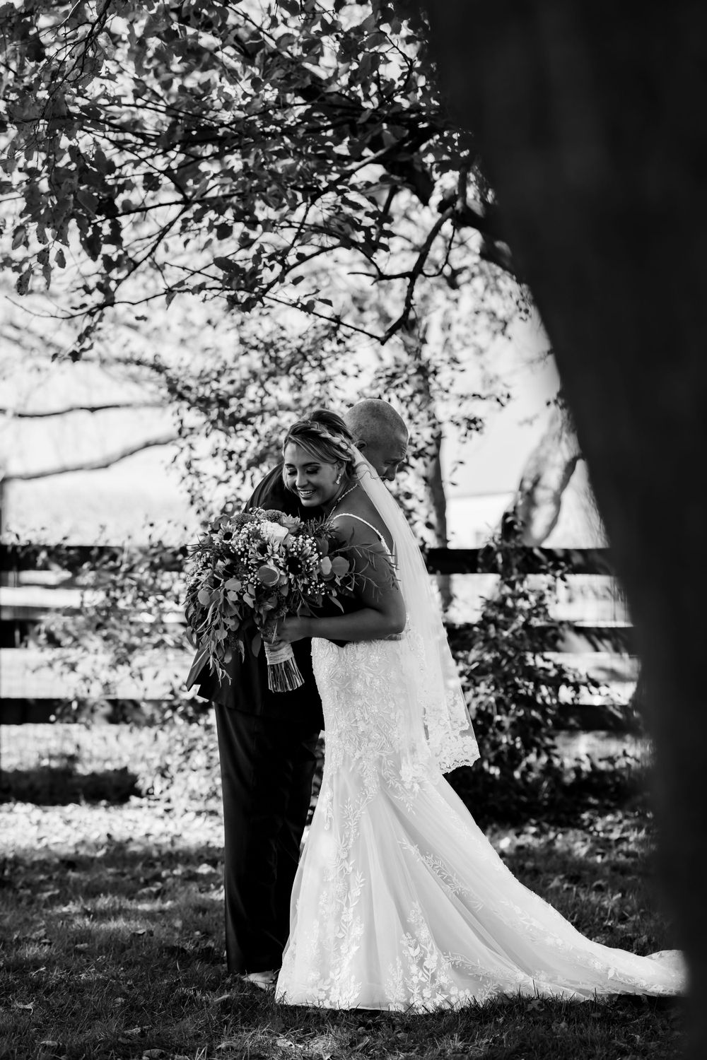 Black and white wedding photo under tree branches with dramatic lighting.