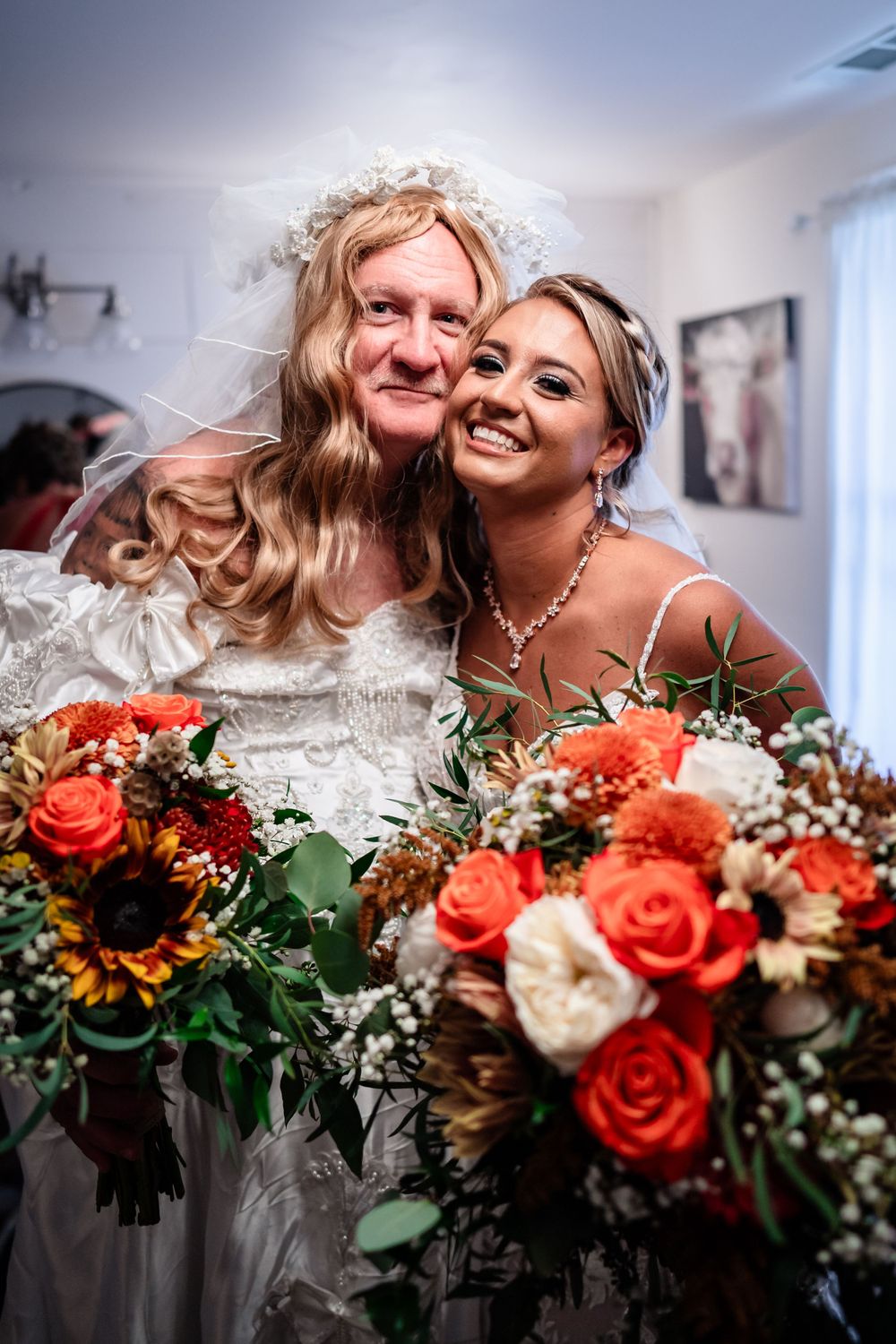 Wedding couple sharing an intimate moment with vibrant coral roses and white floral bouquet in foreground.