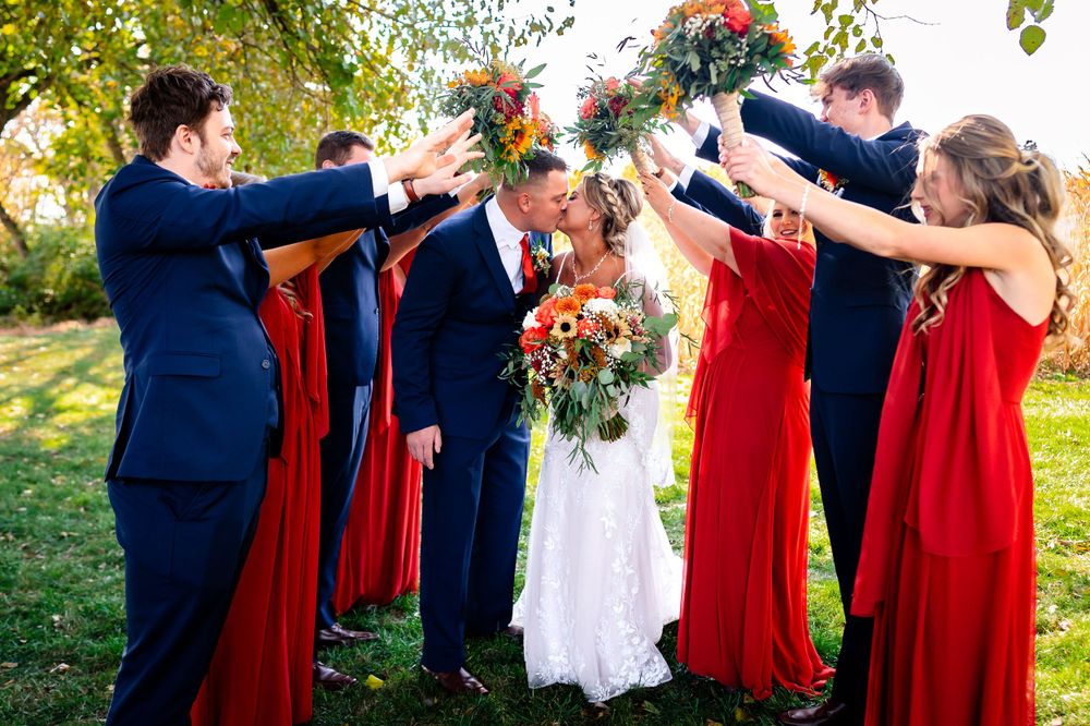 Wedding party in navy and red attire poses playfully with arms outstretched outdoors.