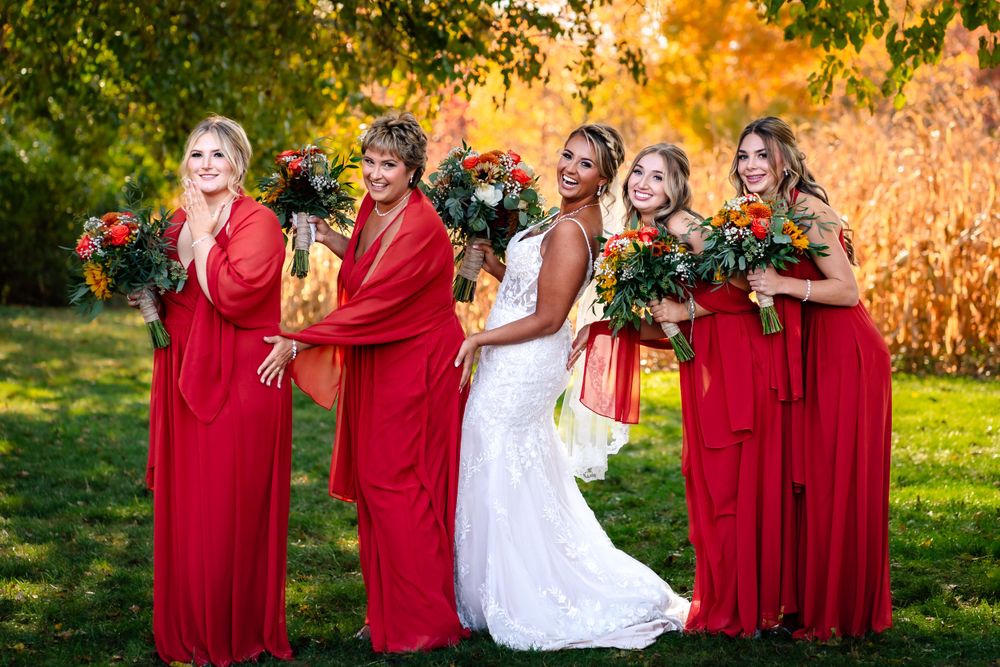 Bridal party in red dresses and white gown celebrates during autumn outdoor photo session.