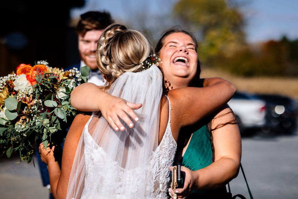 Candid laughter and hugs shared among wedding party members in outdoor setting.