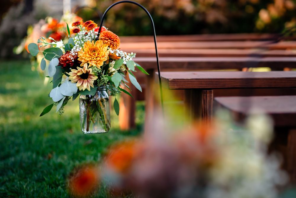 Wedding floral arrangements with orange blooms displayed on wooden benches outdoors.