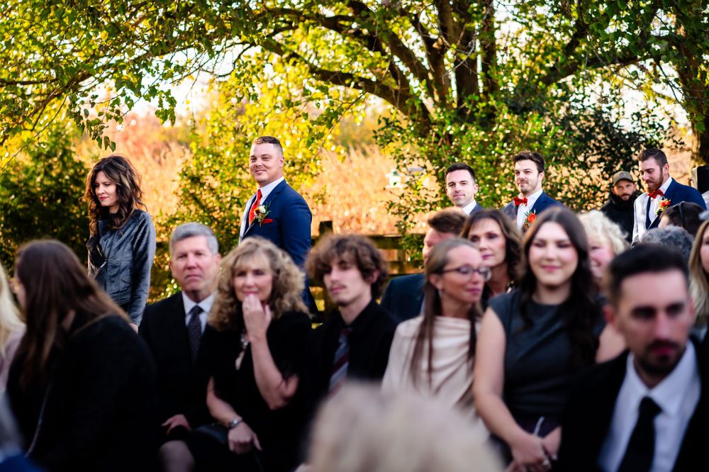 Wedding guests gather under golden autumn trees during outdoor ceremony.