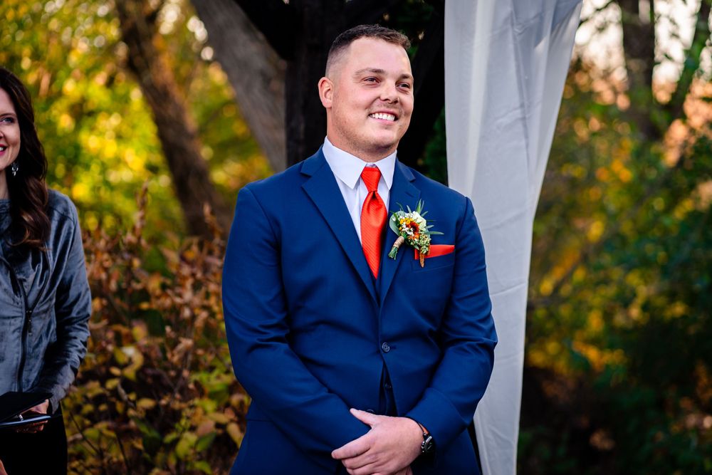Wedding party members in navy suits and red ties stand together during an outdoor autumn ceremony.