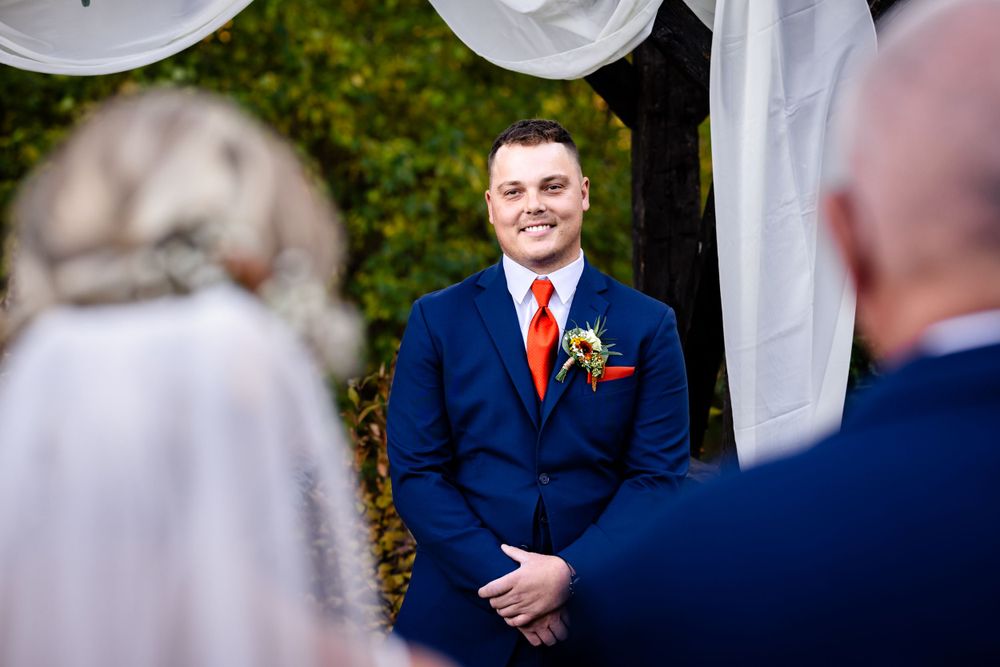Wedding ceremony guests seated outdoors with white chairs and flowing fabric decorations.