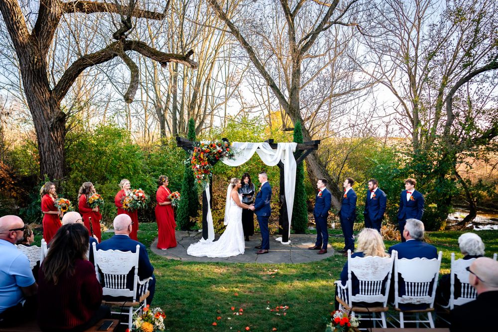 Outdoor wedding ceremony setup with white chairs and fall foliage in the background.