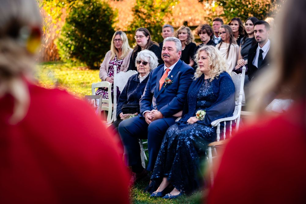 Wedding guests seated in rows of white chairs during an outdoor autumn ceremony.