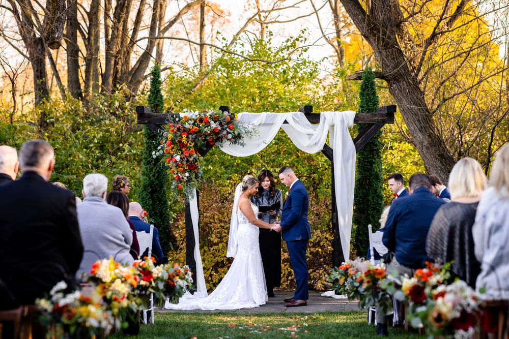 Outdoor wedding ceremony under trees with white draping and floral arrangements.