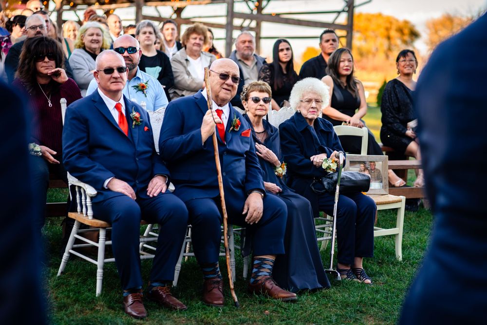Guests watching an outdoor wedding ceremony from white chairs with golden sunlight filtering through.