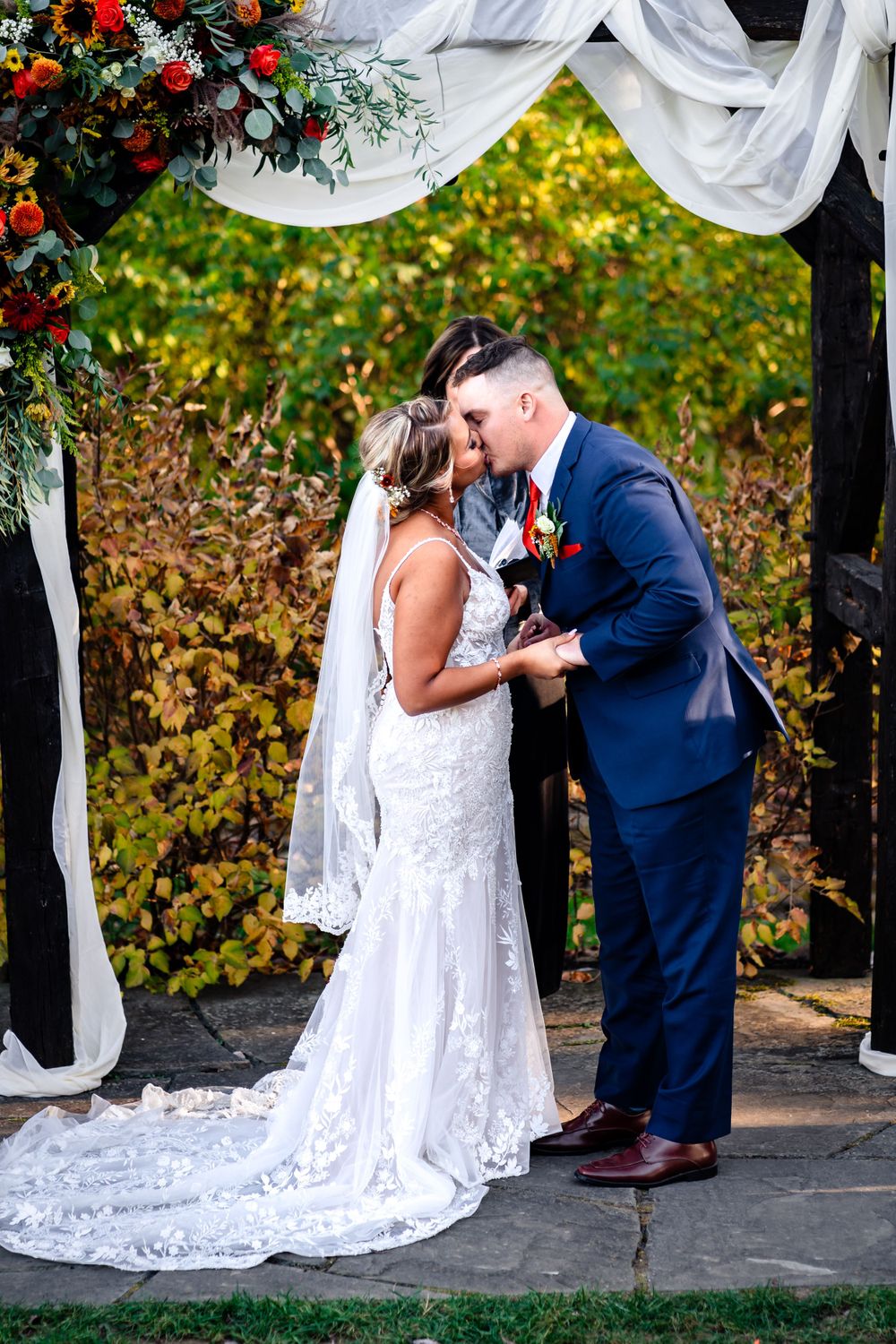Wedding couple sharing intimate moments under a white draped arch with red floral accents.