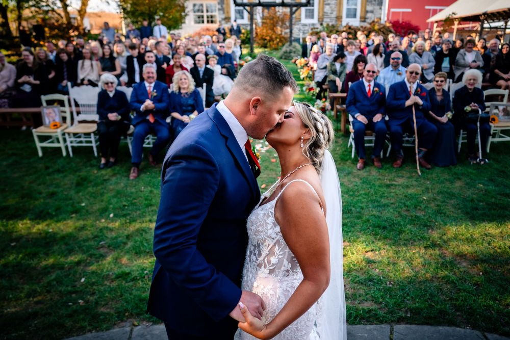 A romantic outdoor wedding ceremony with guests seated on white chairs during golden hour.