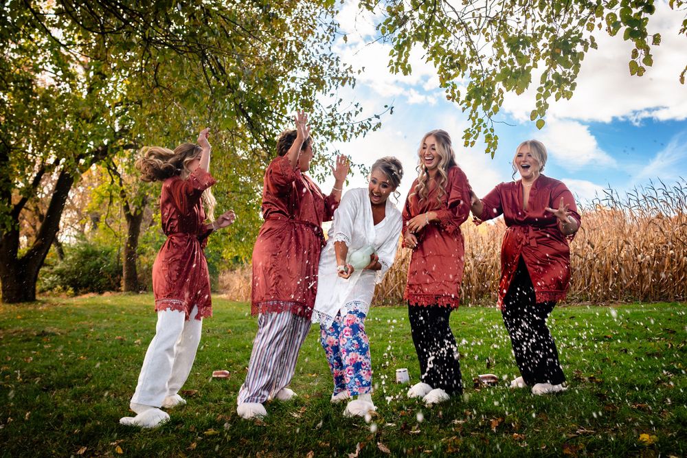 Wedding party in burgundy dresses jumping joyfully in a fall outdoor setting.