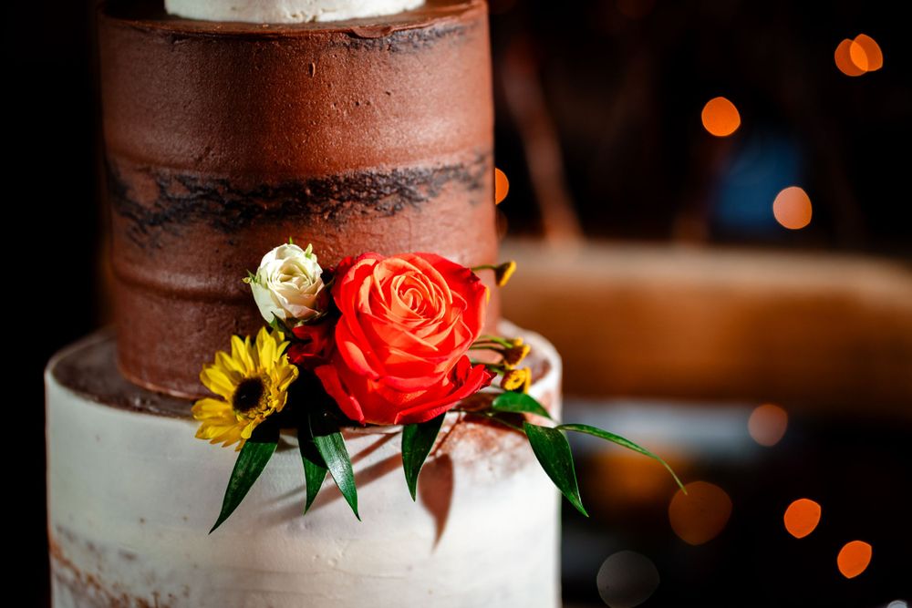 Close-up details of a rustic wedding cake with coral roses and yellow flower accents.