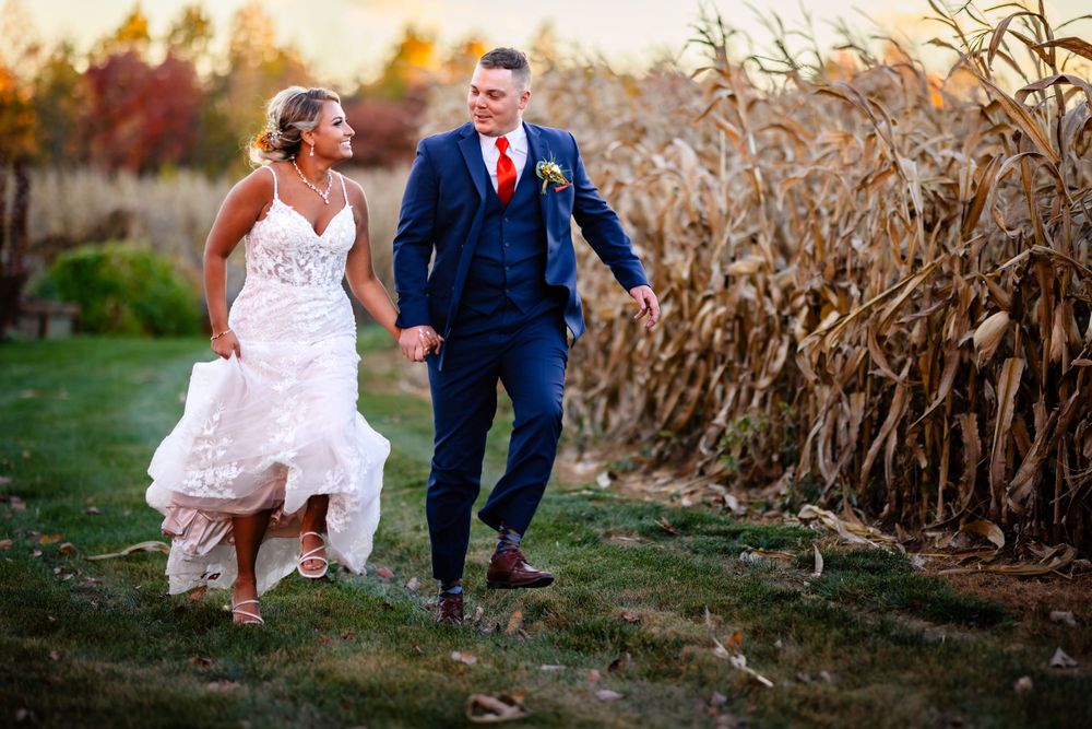Newlyweds walking through dried corn stalks in a farm field at sunset.