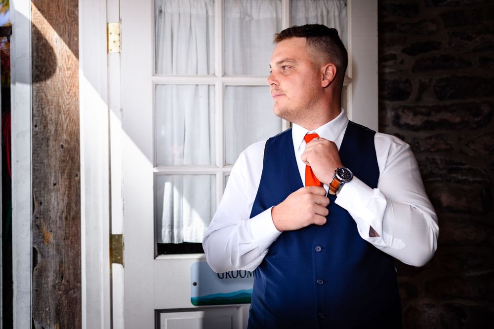 Groomsmen in formal attire getting ready in a rustic room with white walls.
